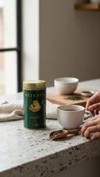 Beteaya tea canister on a kitchen counter with a cup of tea and tea leaves.